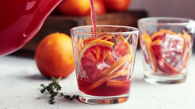 Pouring  red orange juice in a large glass or blood orange sparkling vodka cocktail or aperitif with campari