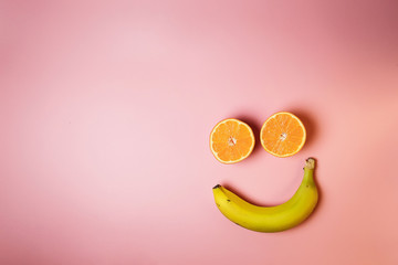Smiley face with two oranges and a banana with copy space on a pink background