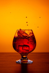 Glass of alcoholic drink Whiskey with ice cubes on wooden table on orange background.