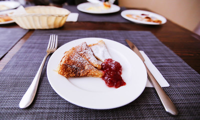 Pancakes with jam and powdered sugar on a white plate. Fresh morning aromatic breakfast.
