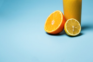 a glass of fresh juce and two paper tubes next to a lemon and an orange on a blue background with copy space