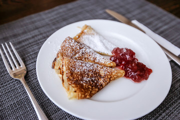 Pancakes with jam and powdered sugar on a white plate. Fresh morning aromatic breakfast.