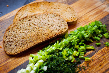 Toasted rye bread and green onions chopped finely with greens on the surface of the cutting board