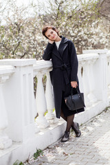 Beautiful young woman in dark woolen coat in the street in the spring time. Almond flowers blossoms,wearing trendy coat.
