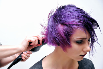 Fototapeta premium A girl in a gray t-shirt and makeup sitting with wet, purple and short hair on a white background in the middle of the frame.