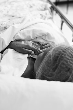A black and white image of a black lady lying in a hospital bed in a theatre waiting are, waiting for her cesarean section