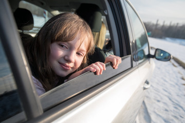 Happy little girl looking through open window in the car