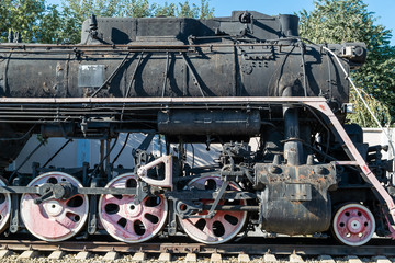 Old rusty steam locomotive beside a railway station platform. Retro train.