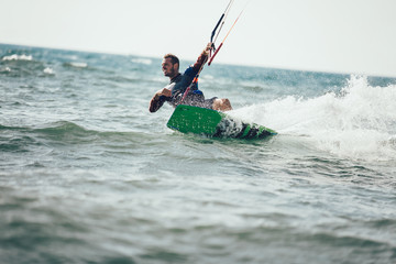 Fototapeta premium Professional kiter makes the difficult trick on a beautiful background. Kitesurfing Kiteboarding action photos man among waves quickly goes