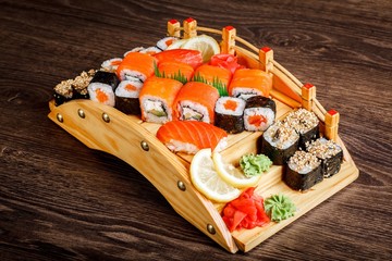 Black and red sushi sashimi set on a wooden bridge on a brown wooden table. With tune, prawn,...