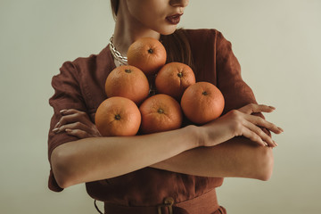 cropped view of stylish girl holding fresh oranges isolated on beige