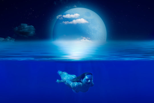 The girl swims under water on a moonlit night. © Viktor