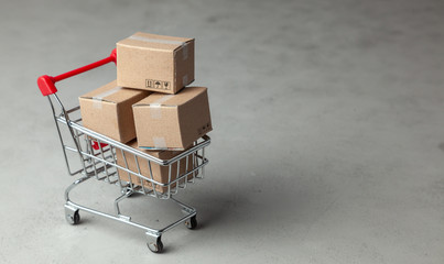 Buying goods in the online store. Cardboard boxes in the shopping basket on gray background.
