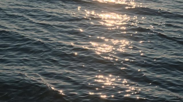 Zeitlupe, slow motion von hellen, sonnigen funkelnden Glitzern auf der Wasseroberfl&auml;che und Wellen im goldenen Abendlicht