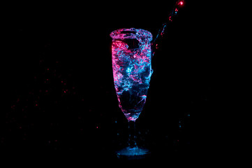 Party glass overflowing with splashing liquid shining in blue and red light isolated on a black background