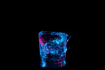 Glass overflowing with blue lit water on a black background