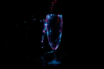 Liquid sparkling in blue and red light and splashing into a champagne flute isolated on a black background