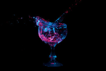 Liquid splashing out of glass under colorful lights on a black background