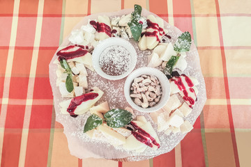 cheese plate with apples, honey and cashews, different types of cheese sprinkled with jam and sprinkled with powdered sugar, bowl of cashews, top view