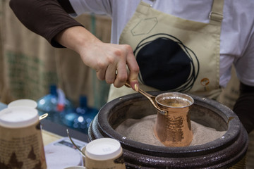 woman making coffee in jezva on the hot sand in special heater