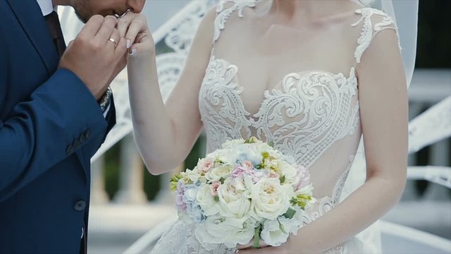 The groom puts the wedding ring on finger of the bride and kisses her hand. The bride and groom exchange wedding rings.