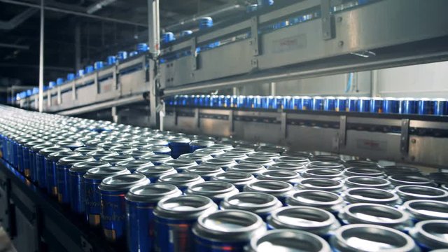 Beer in cans moving on a conveyor at a brewery, close up.