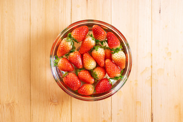 Fresh strawberries in water bowl on wooden table