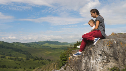 Mother and daughter are sitting on top of mountain
