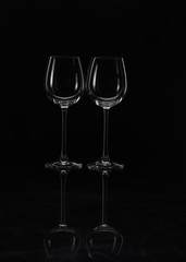 Two wine glasses stand side by side on a black background with beautiful highlights close-up