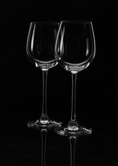 Two wine glasses on a black background with beautiful highlights, one in front of the other; close-up