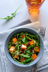 Salad with arugula,pumpkin and pomegranate seeds on gray wooden background. Vegetarian food concept. Selective focus.