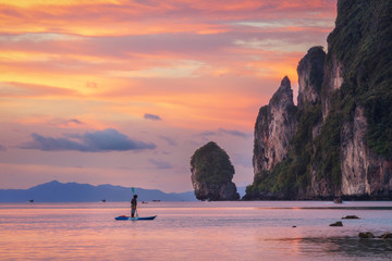 Sunset Phi Phi island Loh Dalum beach with man on SUP board and limestone rocks on background