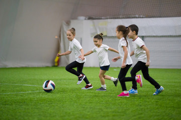 Obraz premium Children playing football indoors. Kids running on the field after the ball