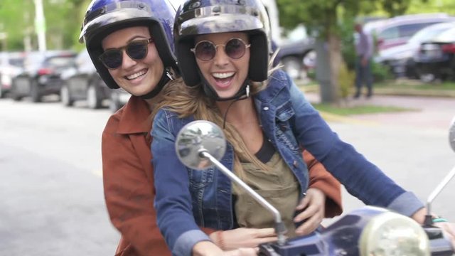 Slow motion of two friends smiling and having fun rriding scooter in city