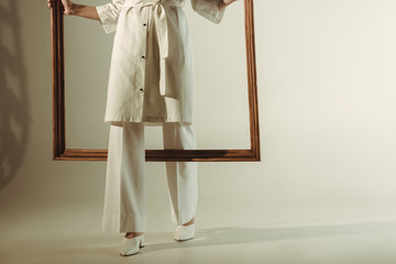 cropped view of woman in white trendy outfit posing with big wooden frame