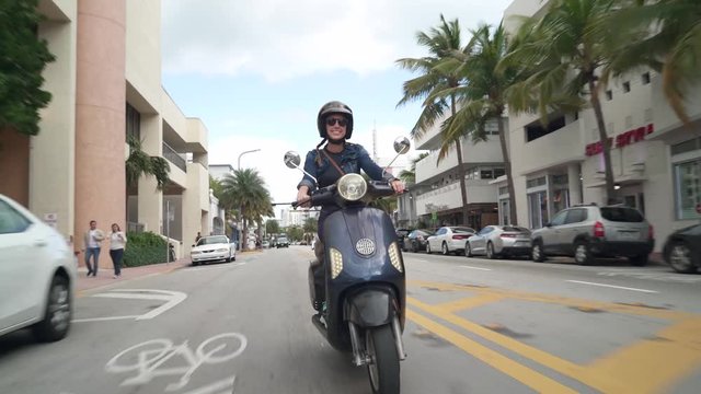 Young woman riding vintage scooter in sunny city