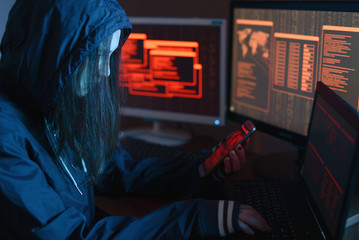 Girl hacker in the hood holding the phone in hands trying to hack the mobile device cloud in the...