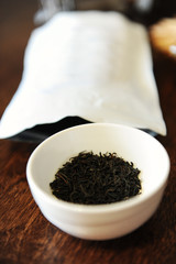 Twisted black tea leaves in a white bowl near the white packaging with free place to design