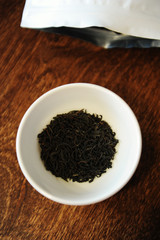 Twisted black tea leaves in a white bowl near the white packaging with free place to design