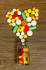 A jar with heart-shaped pills on a wooden background