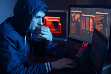 Hacker in a hood thinking about the problem of hacking or malware infection on the background of...