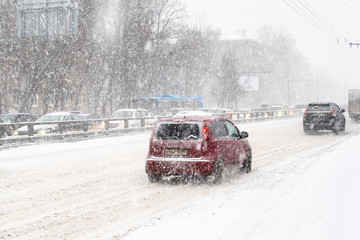 cars drive at snow-covered urban road in snowfall