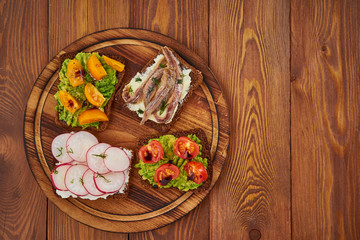 Smorrebrod - traditional Danish sandwiches. Black rye bread with fish, vegetables, copy space, on dark brown wooden background