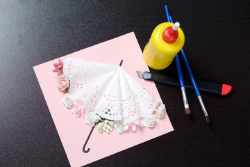 Making greeting card from paper, cardboard and tape. Nearby on the surface are tools for its manufacture.