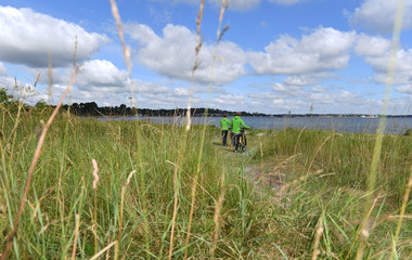 zwei Fahrradfahrer schieben ihre Fahrräder zwischen den Dünen am Strand entlang