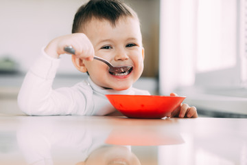 A child in the kitchen eating their own oatmeal with a red plate