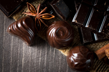 Assortment of dark, white and milk chocolate stack, chips. Chocolate and coffee beans on rustic wooden sacking background. Spices, cinnamon. Selective macro focus. Chocolates background. Sweets