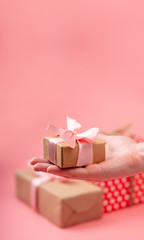 Hands holding gift box Packed in Kraft paper on pink background. Holiday card for Valentine's day and women's day