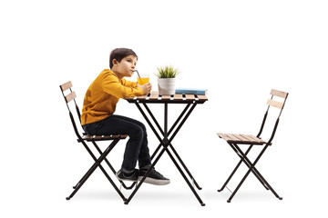 Fototapeta premium Little boy drinking juice and sitting alone at a table