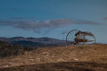 Rusty harrow plow left roadside in Danville Vermont with with blue sky and mountains in background